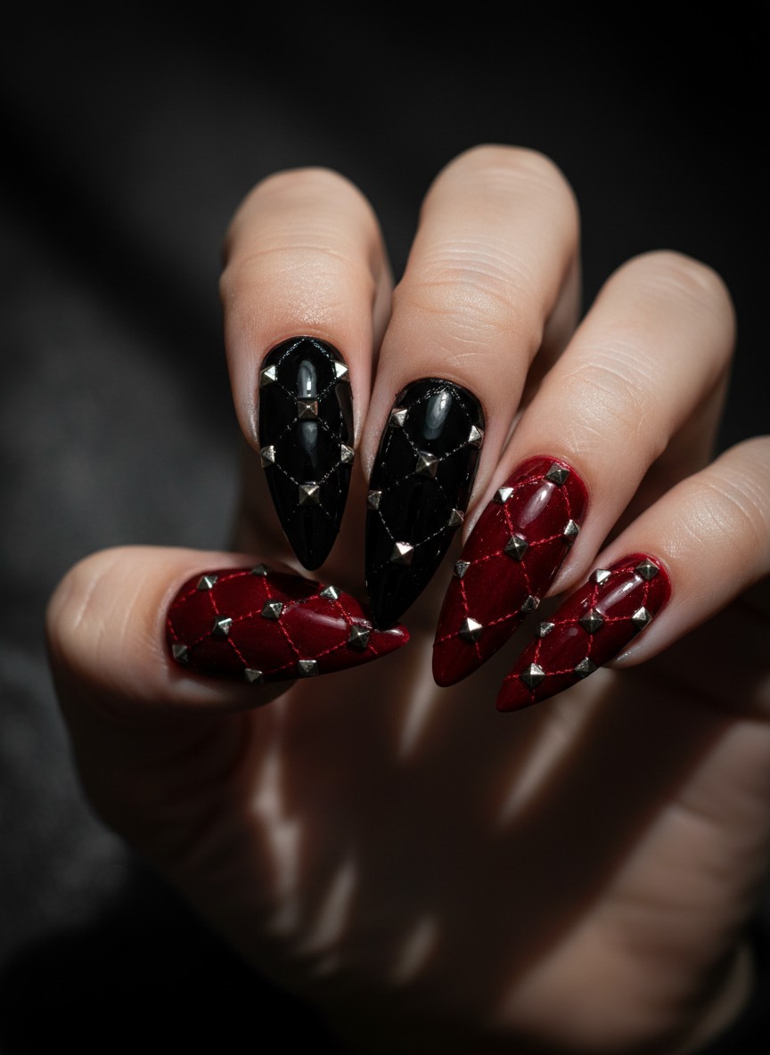 Sharp stiletto nails featuring black and deep red quilted patterns with silver studs in moody lighting.