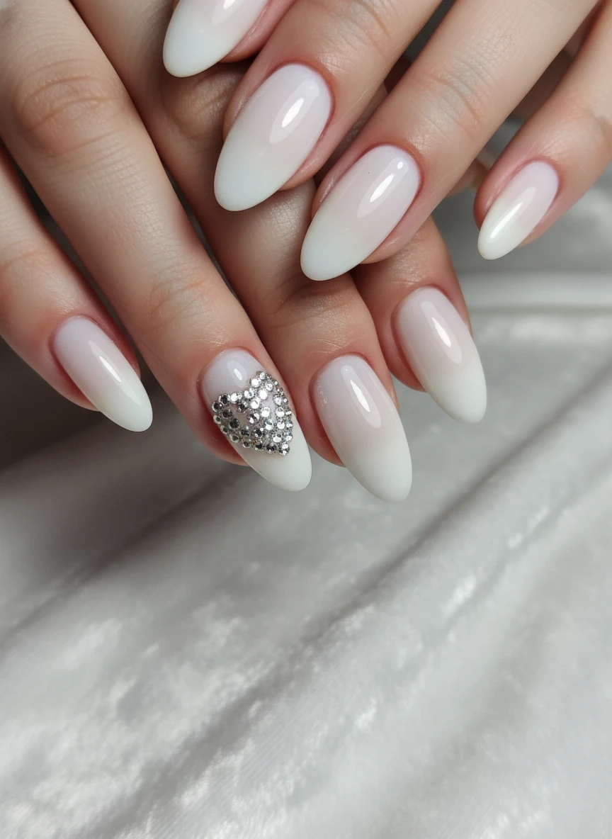 Soft milky white nails featuring a heart motif crafted from sparkling silver rhinestones on the ring finger.